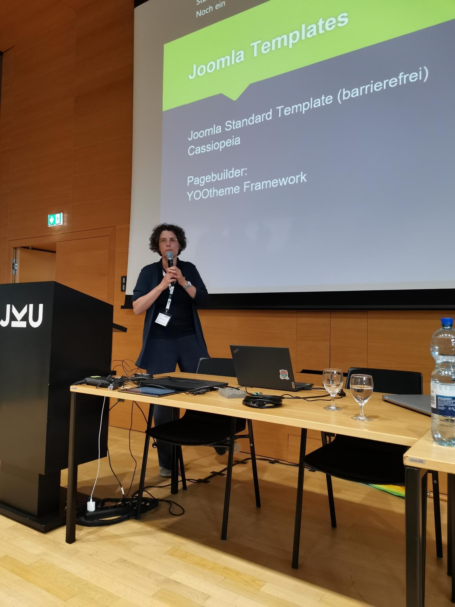 Sigrid Gramlinger steht vor einer Pr&auml;sentationsleinwand zum Thema Barrierefreiheit mit Joomla mit einem Mikrofon in der Hand.