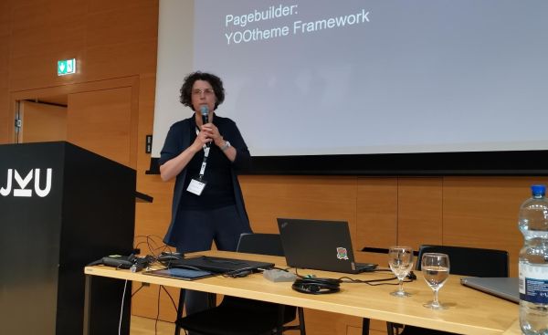 Sigrid Gramlinger steht vor einer Pr&auml;sentationsleinwand zum Thema Barrierefreiheit mit Joomla mit einem Mikrofon in der Hand.